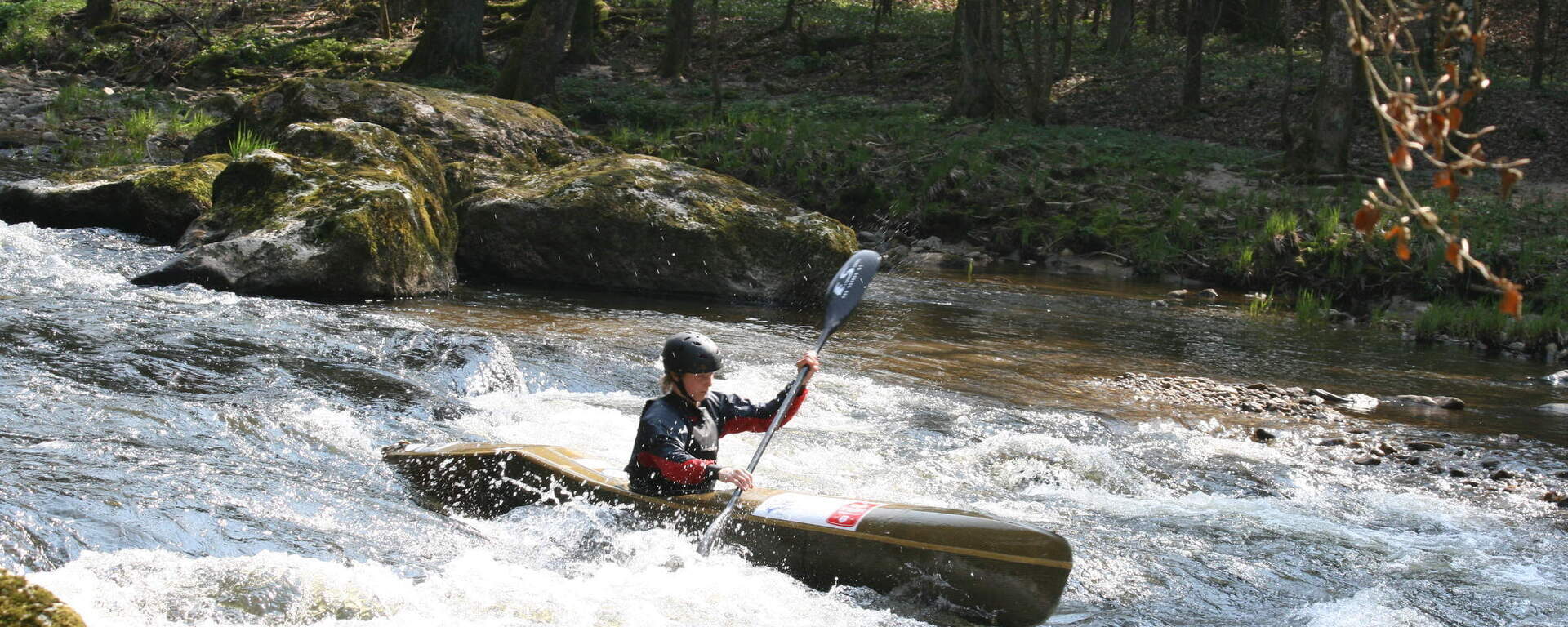 Ein Sportler navigiert gekonnt mit seinem Kajak durch Stromschnellen inmitten der Natur von Bodenmais.