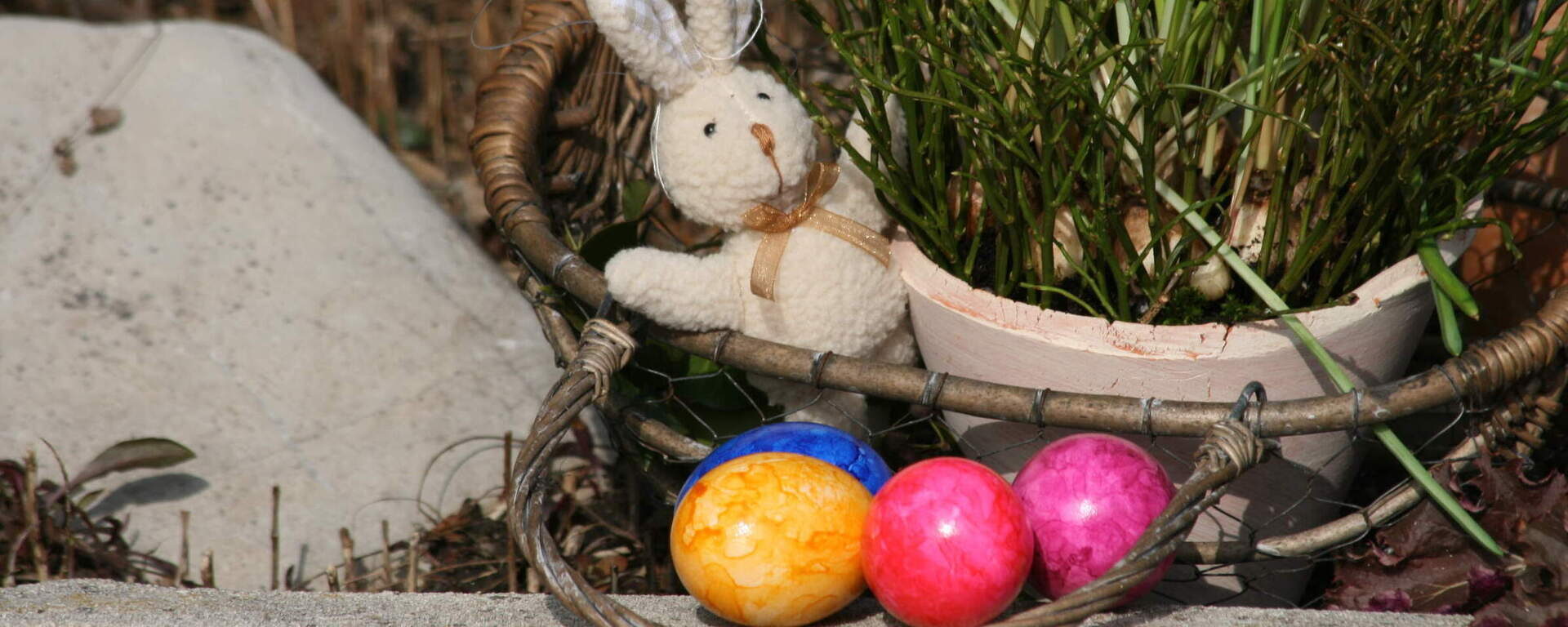 Ein dekorativer Weidenkorb mit bunten Ostereiern und einem Osterhasen liegt am Boden.