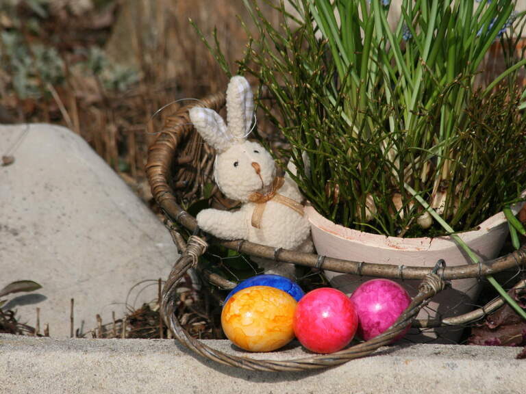 Ein dekorativer Weidenkorb mit bunten Ostereiern und einem Osterhasen liegt am Boden.